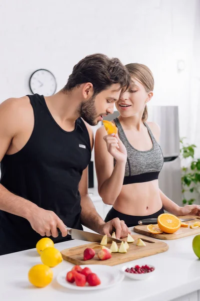 Selective focus of sportive girl feeding bearded man with orange — Stock Photo