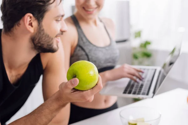 Foyer sélectif de l'homme heureux tenant pomme et regardant ordinateur portable près de la femme — Photo de stock