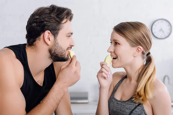 Side view of happy man and woman eating apples and looking at each other — Stock Photo