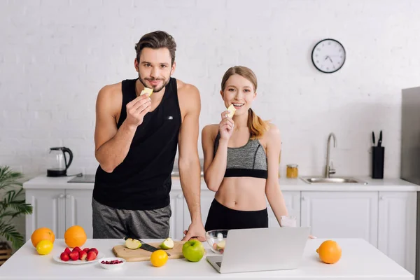 Happy man and woman holding sliced apples near fruits and laptop — Stock Photo