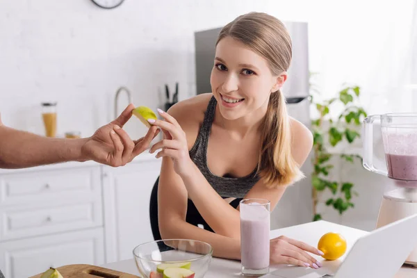 Homme donnant pomme tranchée à la femme près d'un ordinateur portable et verre de smoothie — Photo de stock