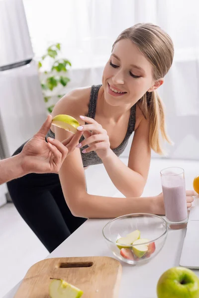 Man giving sliced apple to happy woman near glass of smoothie — Stock Photo