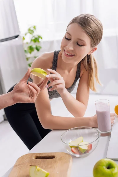 Hombre dando en rodajas de manzana a la mujer feliz cerca de vaso de batido - foto de stock