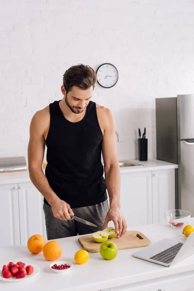 Schöner Mann mit Messer in der Nähe von Obst und Laptop — Stockfoto