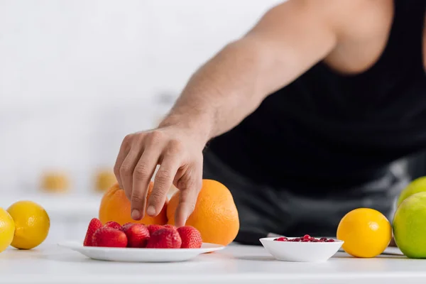 Vista recortada del hombre alcanzando fresas rojas cerca de frutas - foto de stock