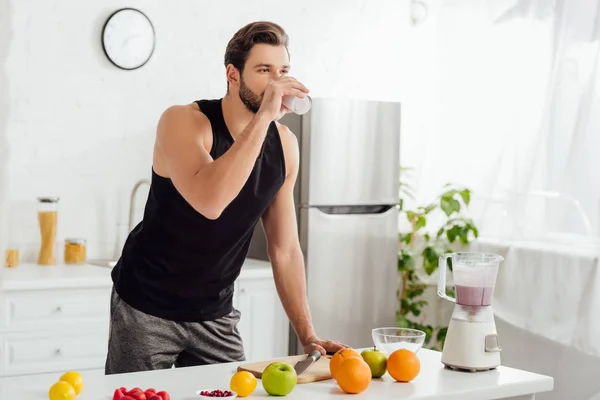 Uomo barbuto bere frullato fresco vicino frullatore e frutta — Foto stock