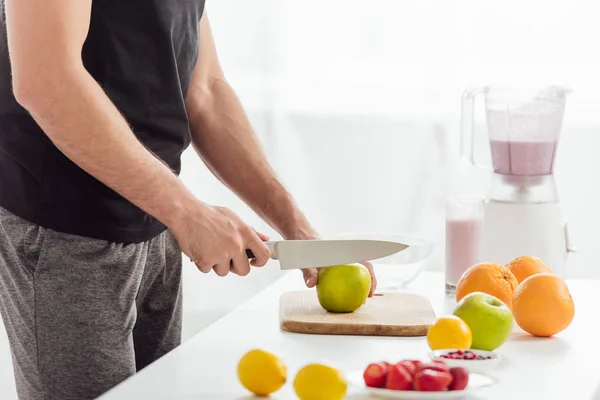 Vista ritagliata dell'uomo taglio mela vicino a frutta fresca e frullato — Foto stock