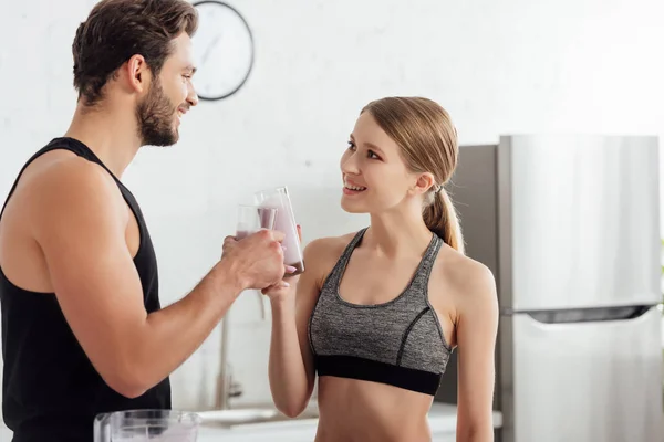 Feliz hombre y mujer tintineo gafas con smoothie y mirando el uno al otro - foto de stock