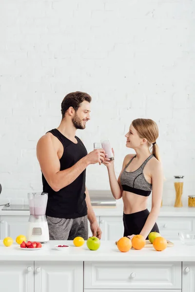 Вид сбоку на счастливых мужчину и девушку, кликающих бокалы с смузи рядом с фруктами — стоковое фото