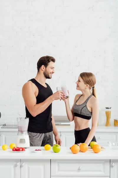 Vista lateral de feliz hombre y chica tintineo gafas con smoothie cerca de frutas - foto de stock