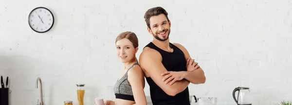 Panoramaaufnahme eines athletischen Mannes mit verschränkten Armen neben einer glücklichen Frau mit Smoothie im Glas — Stockfoto