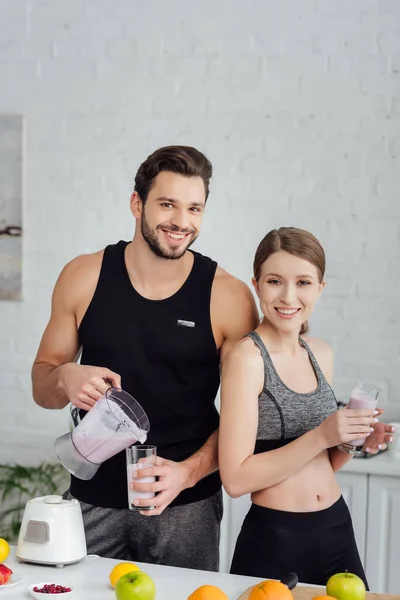 Athletic man pouring smoothie in glass near happy woman with drink — Stock Photo