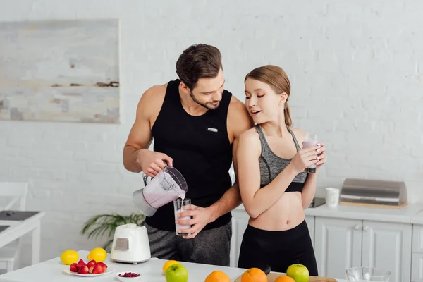 Athletic man pouring smoothie in glass near attractive woman — Stock Photo