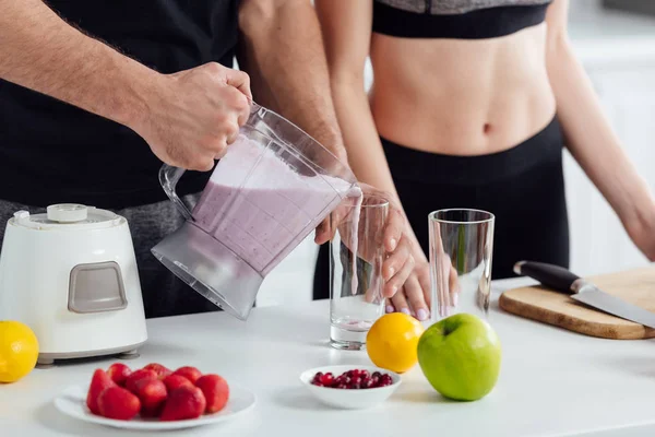 Cropped view of man pouring smoothie in glass near sportive girl — Stock Photo