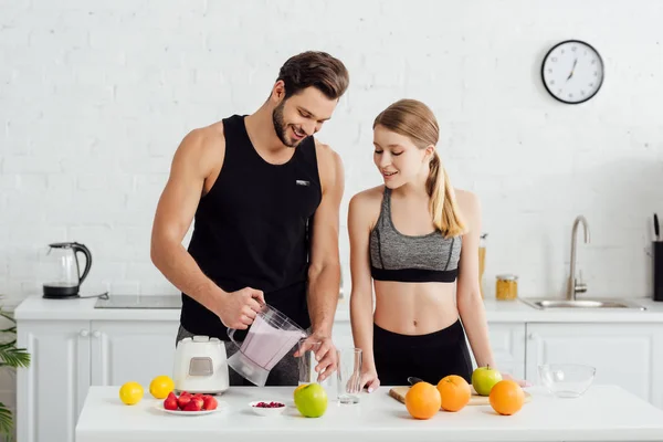 Uomo sportivo che tiene frullatore con frullato vicino ragazza felice e frutta — Foto stock