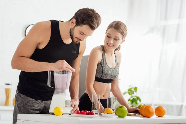 Спортивный человек готовит смузи рядом счастливая девушка и фрукты — стоковое фото
