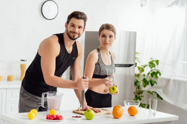 Homem feliz segurando faca perto de menina esportiva e liquidificador com smoothie — Fotografia de Stock