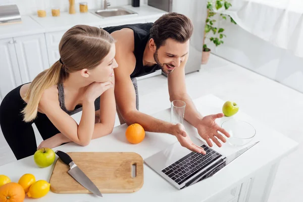 Overhead view of happy man gesturing near laptop and sportive girl — Stock Photo