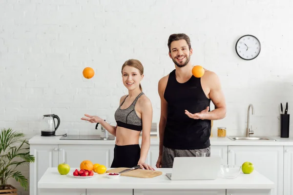 Sportive girl and cheerful man throwing in air oranges near laptop — Stock Photo