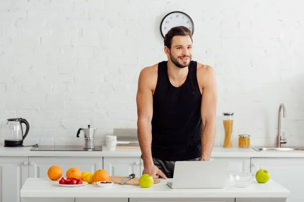 Uomo felice sorridente vicino a frutta fresca e laptop — Foto stock