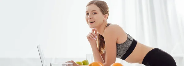 Plano panorámico de chica feliz cerca de la computadora portátil y frutas - foto de stock