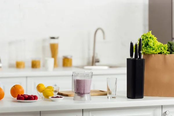 Frutas sabrosas y maduras cerca de smoothie y bolsa de papel con lechuga en la cocina moderna - foto de stock