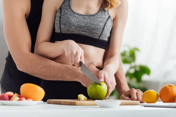 Vista recortada de pareja de corte de manzana en la tabla de cortar - foto de stock