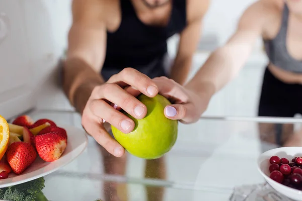 Vista recortada de hombre y mujer tocando manzana en nevera - foto de stock