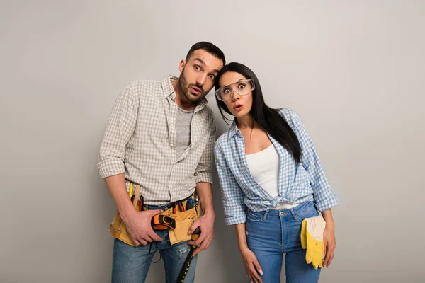 Shocked manual workers in goggles with tool belt on grey — Stock Photo