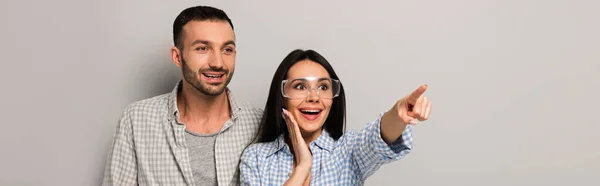 Panoramaaufnahme aufgeregter Arbeiter in Schutzbrille mit Werkzeuggürtel, der auf grau zeigt — Stockfoto