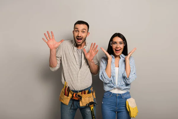 Excited manual workers in goggles with tool belt on grey — Stock Photo