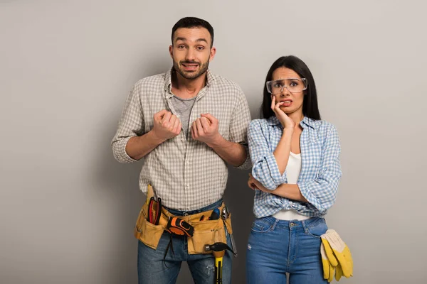 Worried manual workers in goggles with tool belt on grey — Stock Photo