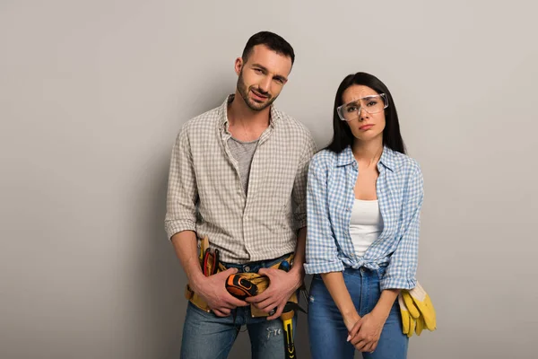 Emotionale Handarbeiter in Schutzbrille mit Werkzeuggürtel auf grau — Stockfoto