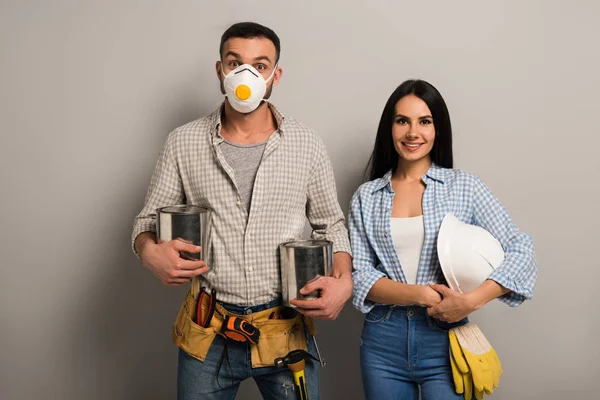 Happy manual workers in safety mask holding paint cans and helmet on grey — Stock Photo