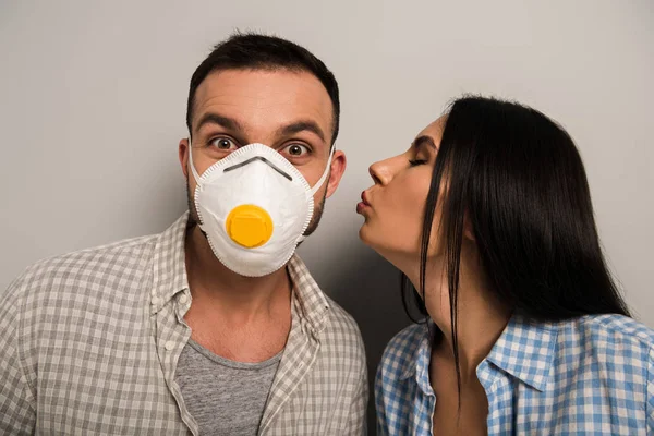 Жінка цілує щасливого працівника в масці безпеки на сірому — стокове фото
