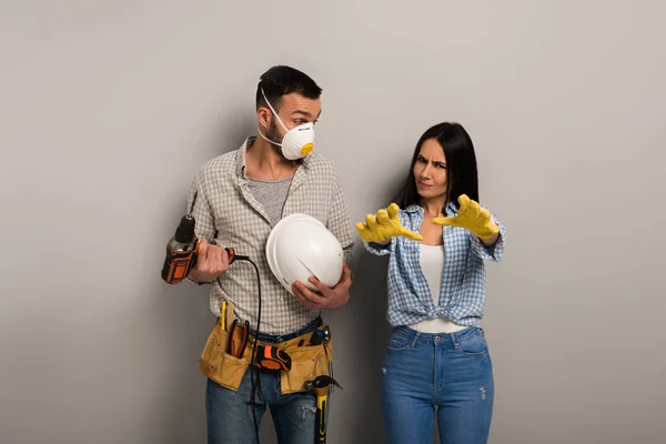 Emotional manual workers in safety mask holding electric drill and helmet on grey — Stock Photo