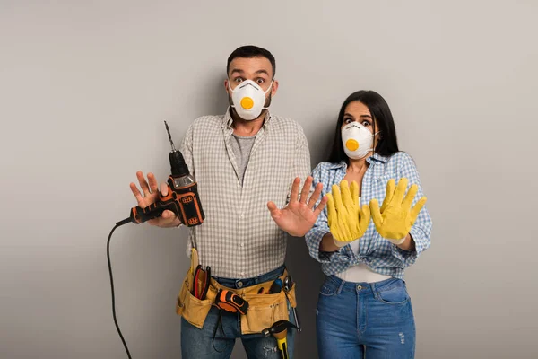 Frightened manual workers in safety masks holding electric drill on grey — Stock Photo