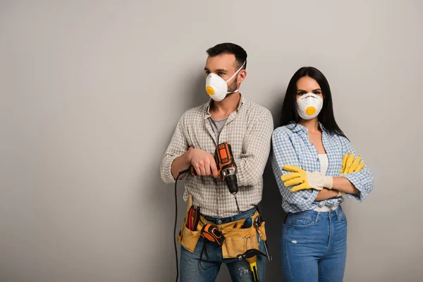 Confident manual workers in safety masks holding electric drill on grey — Stock Photo