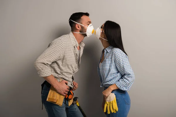 Happy manual workers kissing in safety masks on grey — Stock Photo