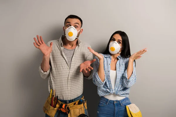 Confusos trabajadores manuales con máscaras de seguridad con gesto de encogimiento en gris - foto de stock