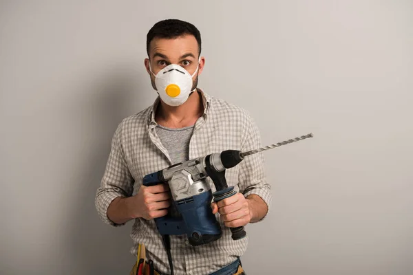 Reparador en máscara de seguridad celebración de taladro eléctrico en gris - foto de stock