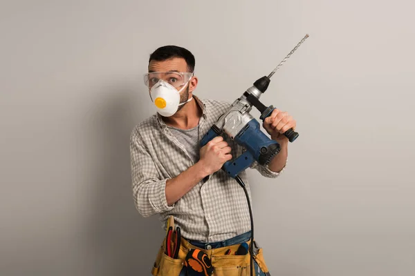 Surprised foreman in safety mask holding electric drill on grey — Stock Photo