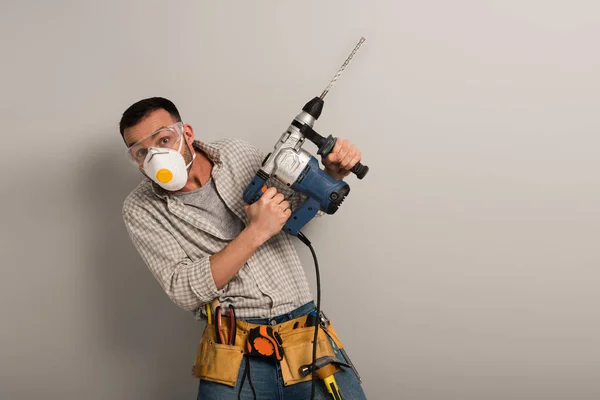 Scared workman in safety mask holding electric drill on grey — Stock Photo