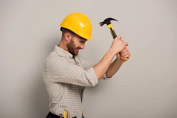 Stressed workman beating yellow helmet with hammer on grey — Stock Photo