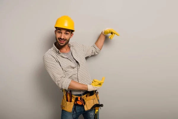 Operaio manuale eccitato in hardhat e guanti di sicurezza che punta sul grigio — Stock Photo