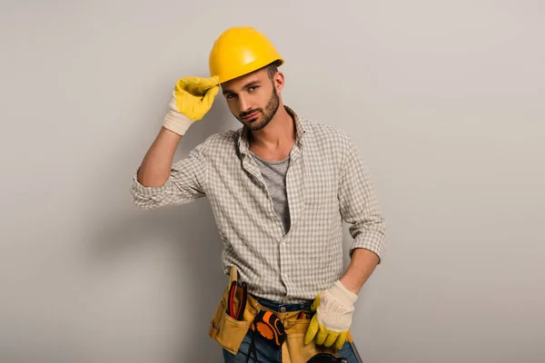 Reparador confiante em capacete e luvas com cinto de ferramentas em cinza — Fotografia de Stock