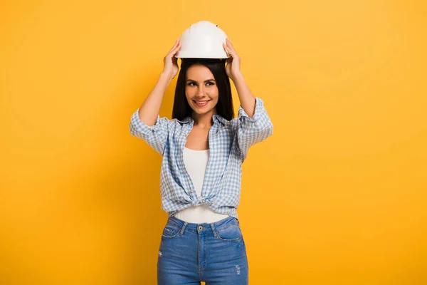 Beautiful smiling female manual worker wearing helmet on yellow — Stock Photo