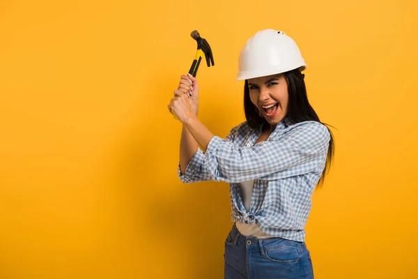 Excited female manual worker in helmet holding hammer on yellow — Stock Photo