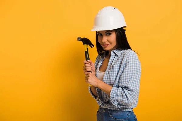 Привлекательная женщина ручной работы в шлеме держит молоток на желтом — стоковое фото