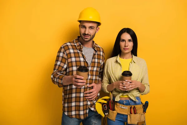 Professional manual workers holding cups with coffee to go on yellow — Stock Photo